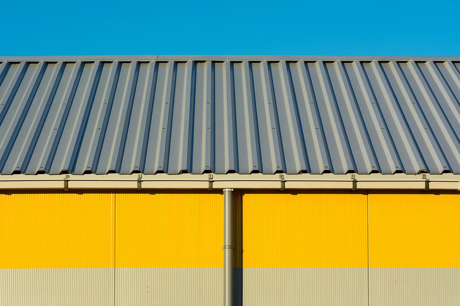 Photo of a yellow warehouse wall with a corrugated metal roof under a clear blue sky.